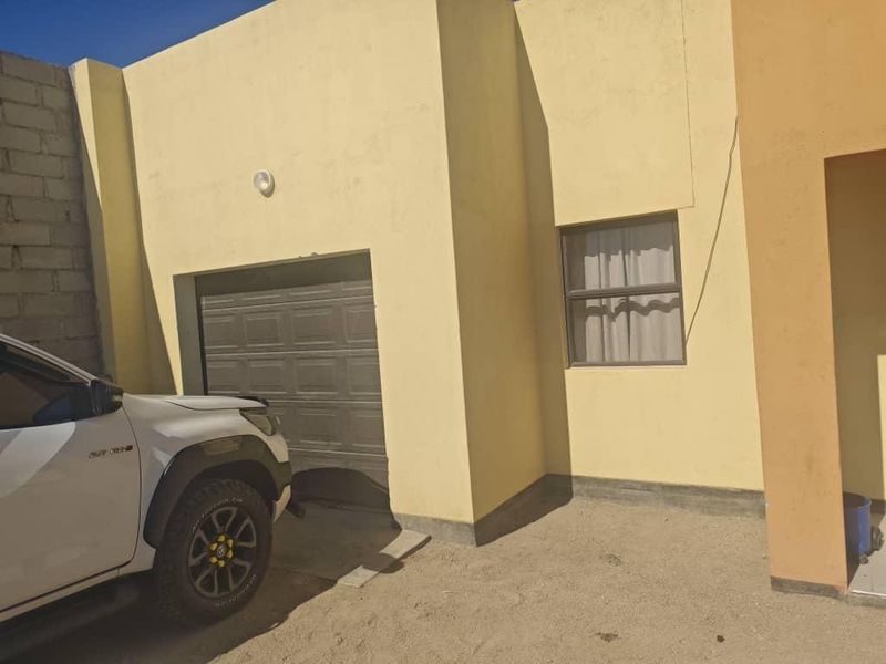 Front exterior view of the property featuring a single garage door and a window, with an unpaved driveway area.