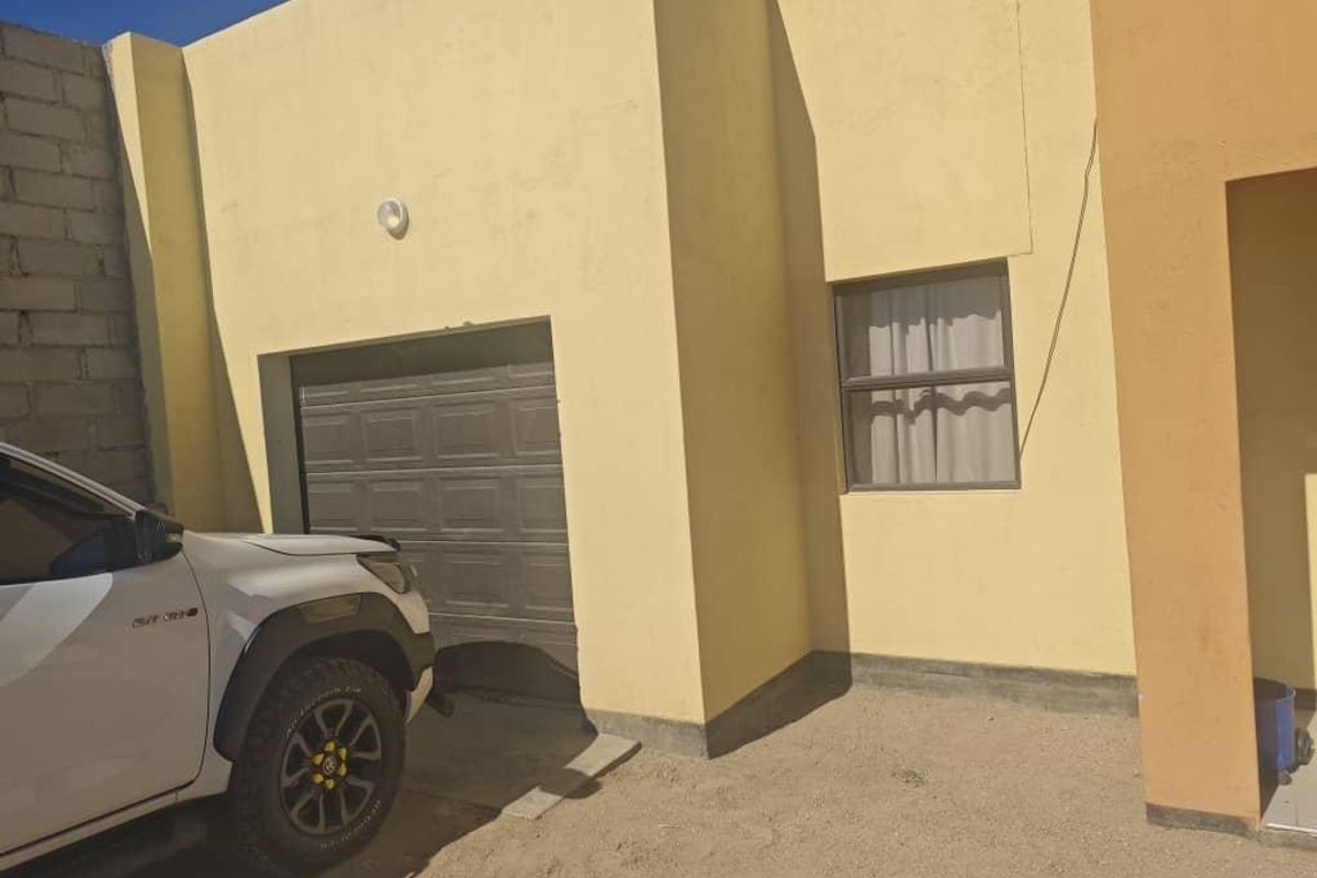Front exterior view of the property featuring a single garage door and a window, with an unpaved driveway area.