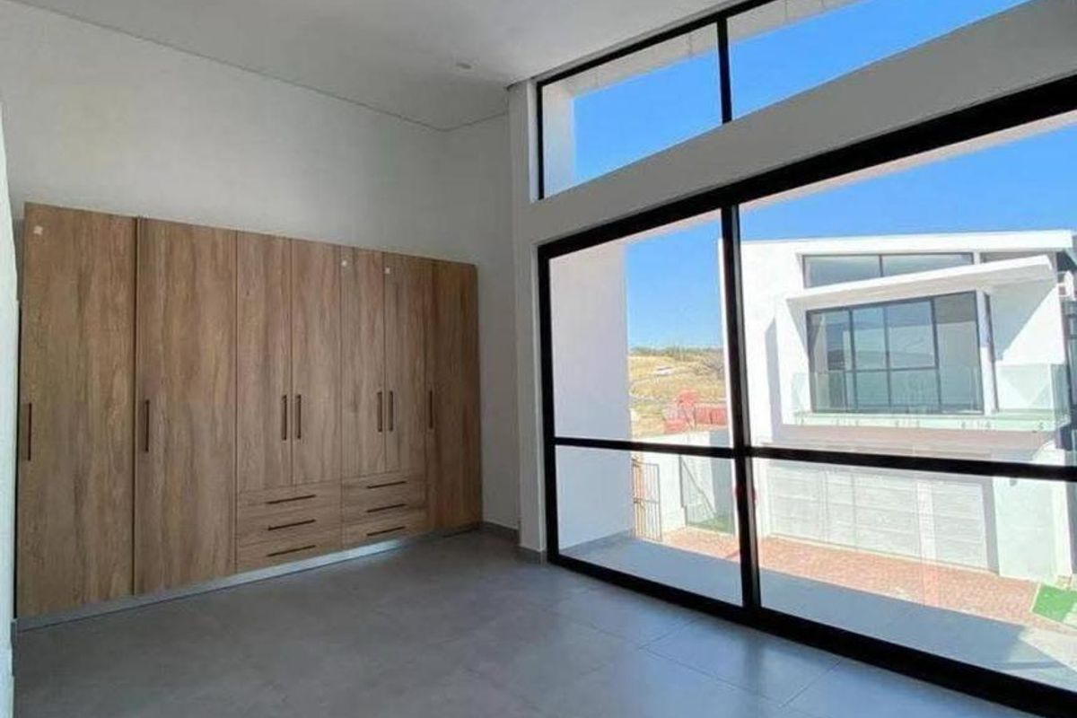 Modern bedroom featuring large format floor tiles, extensive built-in wooden cupboards, and expansive floor-to-ceiling glass doors providing abundant natural light and outdoor access.
