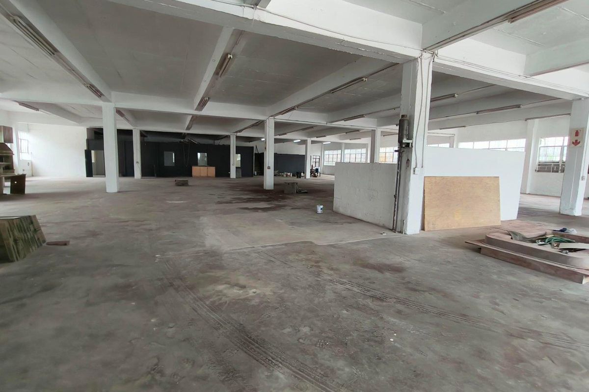 Expansive open-plan industrial warehouse space featuring high ceilings with exposed beams, concrete flooring, and large industrial windows providing ample natural light.