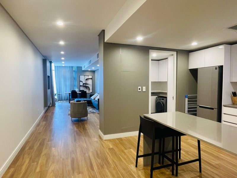 Modern open-plan living area featuring laminate flooring, recessed lighting, and a sleek kitchen with an island, leading into a functional scullery space.