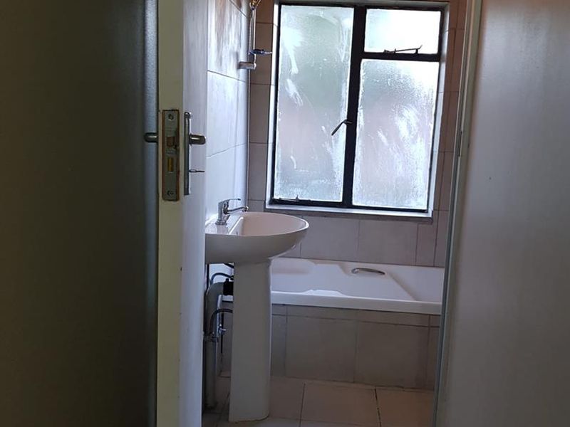 A functional bathroom featuring a pedestal basin, built-in bathtub, and tiled finishes, viewed from the doorway.