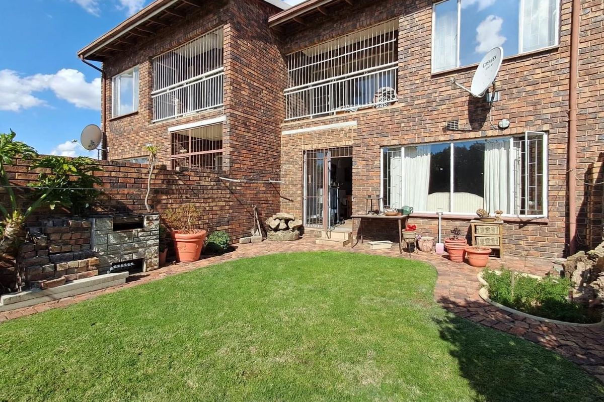Rear view of a face brick townhouse featuring a private garden, paved patio area, built-in braai, and upper-level balcony with security bars.