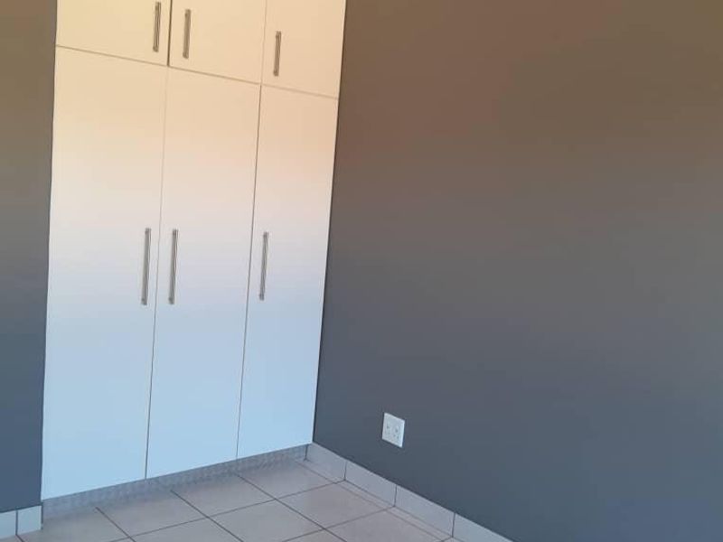 A clean, empty bedroom featuring neutral grey walls, white built-in cupboards, and light-colored floor tiles.