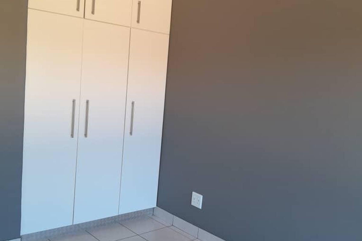 A clean, empty bedroom featuring neutral grey walls, white built-in cupboards, and light-colored floor tiles.