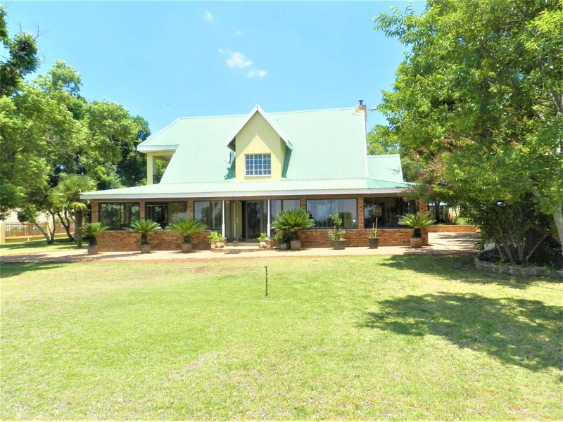 Rear view of a farm-style residence featuring a metal roof, brick exterior, and an enclosed patio overlooking a spacious lawn.