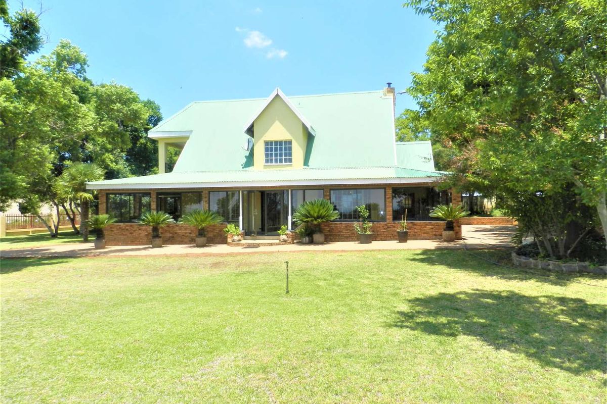Rear view of a farm-style residence featuring a metal roof, brick exterior, and an enclosed patio overlooking a spacious lawn.