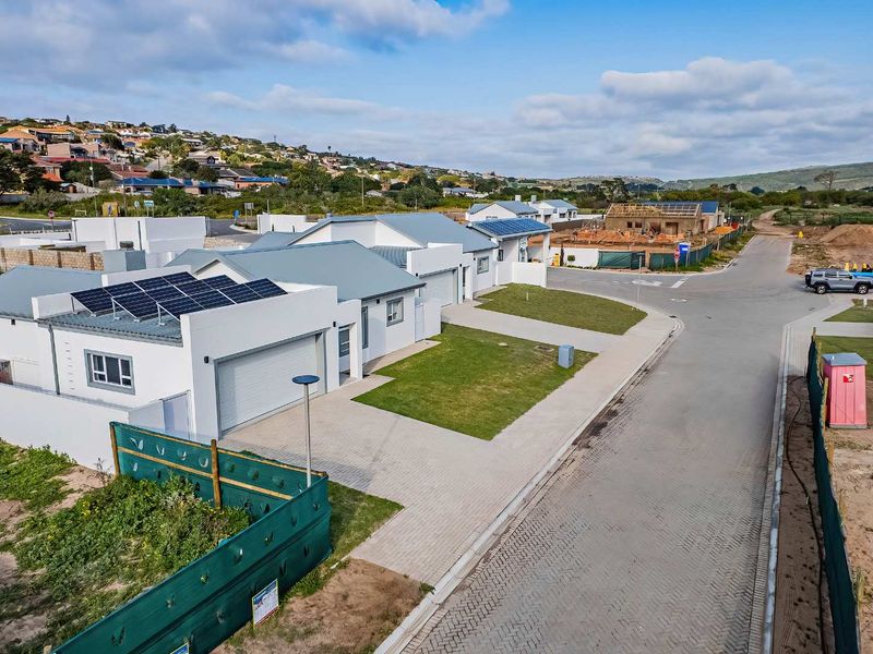 Aerial view of a modern residential property featuring a paved driveway, garage, and roof-mounted solar panels within a developing estate.