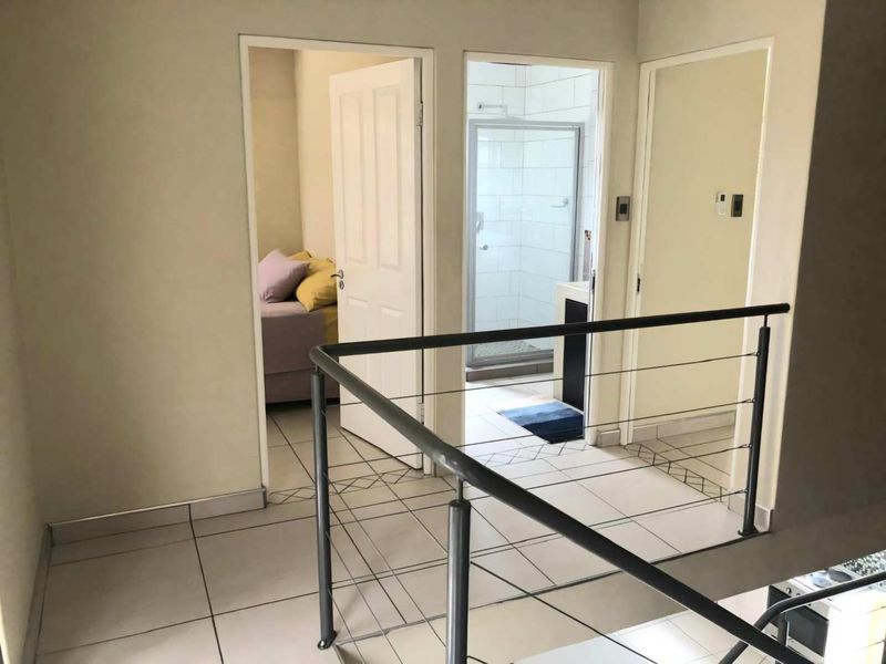 A bright upstairs landing area featuring tiled flooring and a modern metal balustrade, providing access to a bedroom and a bathroom.