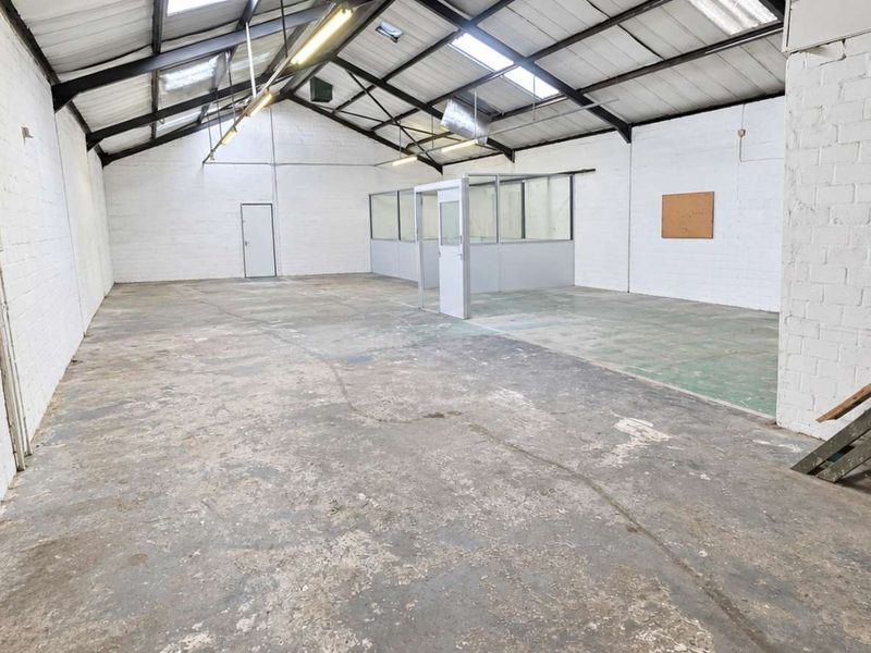 Spacious industrial-style office unit featuring exposed roof trusses, skylights, concrete flooring, and a partitioned office enclosure, offering a versatile open-plan workspace.