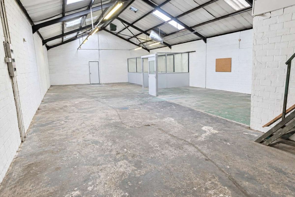 Spacious industrial-style office unit featuring exposed roof trusses, skylights, concrete flooring, and a partitioned office enclosure, offering a versatile open-plan workspace.