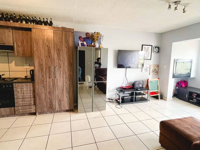 Open-plan living area featuring a compact kitchen with wood-finish cabinetry, integrated appliances, and neutral tiled flooring throughout the space.