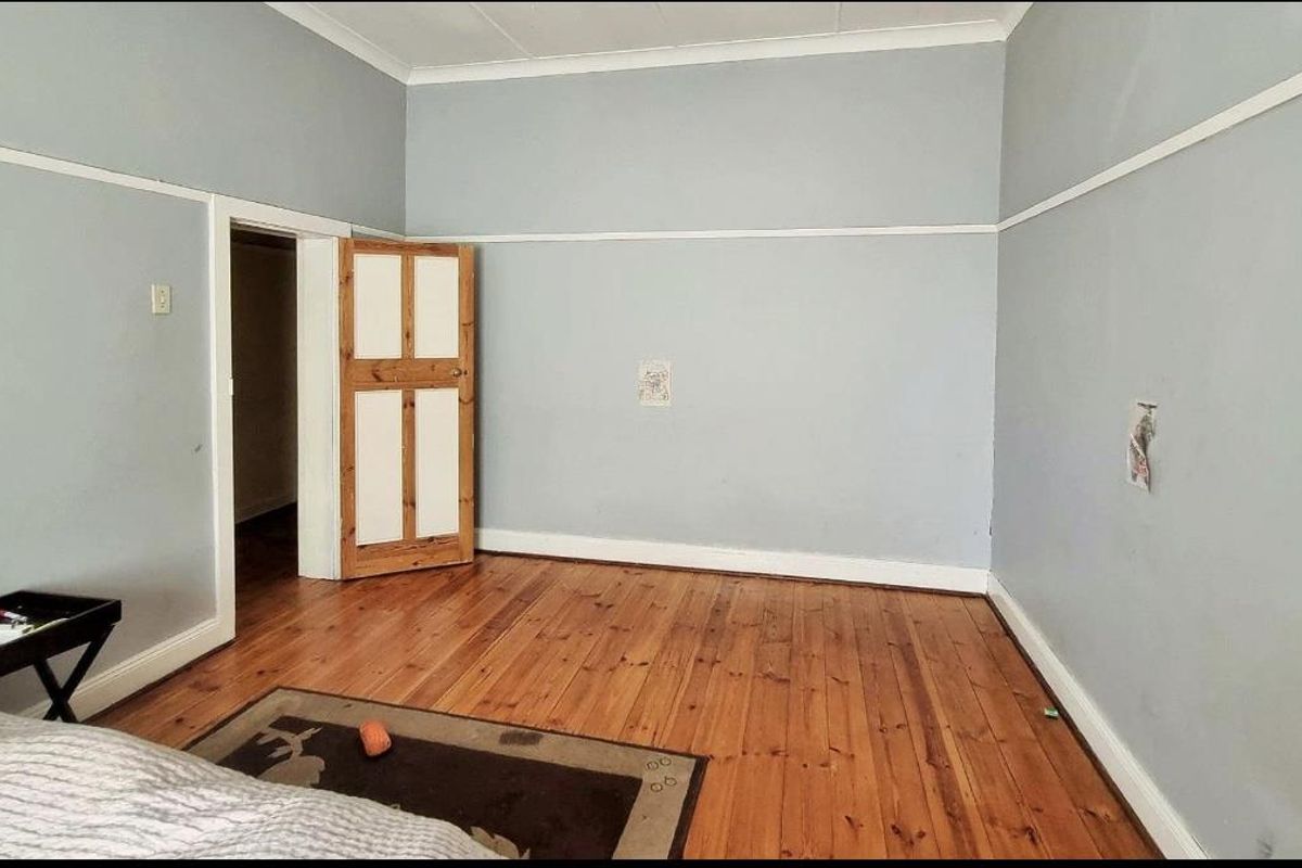 A spacious bedroom featuring polished timber flooring, high ceilings with picture rails, and a traditional wooden door.