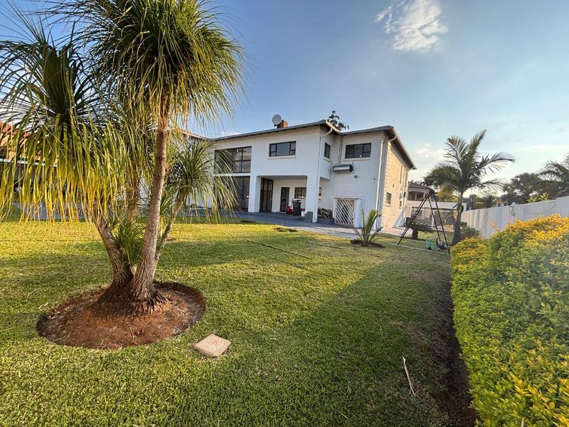 Rear view of a two-story residential house featuring a spacious lawn, paved patio area, and established garden landscaping.