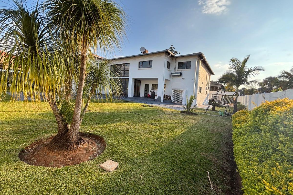 Rear view of a two-story residential house featuring a spacious lawn, paved patio area, and established garden landscaping.