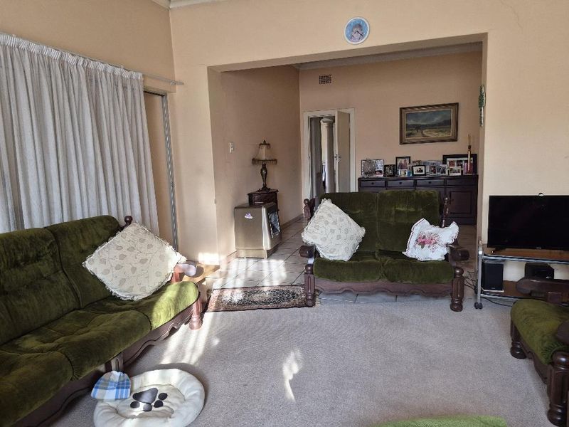 A spacious living area featuring a mix of carpet and tile flooring, connected to an adjacent room via a wide archway.