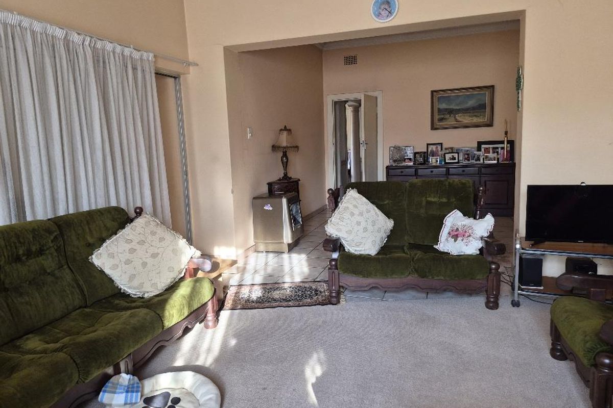 A spacious living area featuring a mix of carpet and tile flooring, connected to an adjacent room via a wide archway.