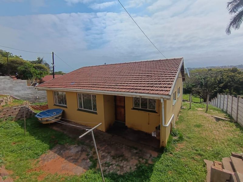 Rear view of a detached house featuring a tiled roof, security-barred windows, and a paved patio area set within a grassed yard.