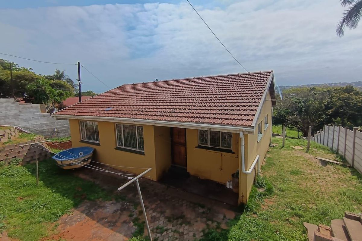 Rear view of a detached house featuring a tiled roof, security-barred windows, and a paved patio area set within a grassed yard.