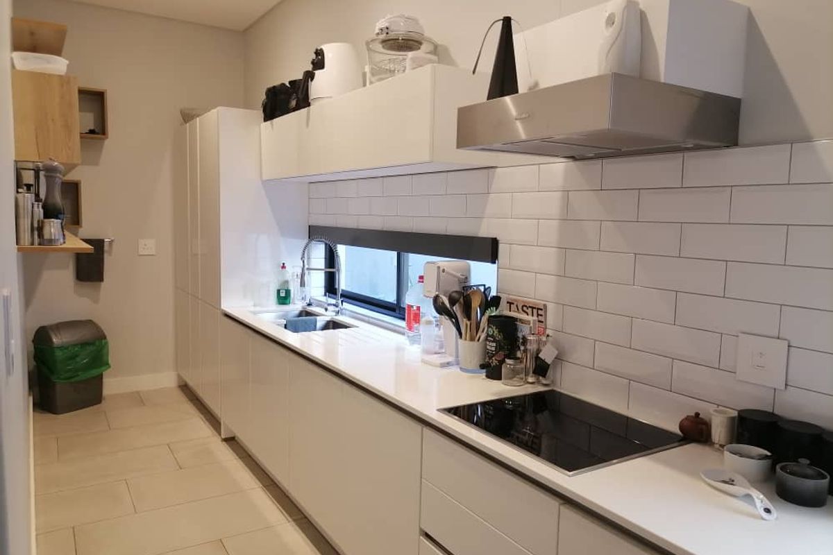 Modern kitchen featuring sleek white cabinetry, stone countertops, a subway tile backsplash, integrated stainless steel extractor fan, and a built-in induction cooktop.