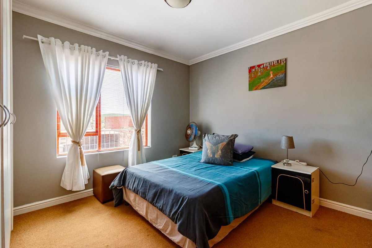 A well-lit bedroom featuring neutral grey walls, carpeted flooring, and a built-in wardrobe, offering a comfortable and functional living space.