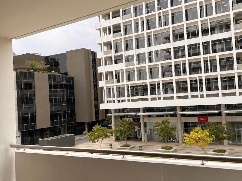 A clean, covered balcony featuring a metal balustrade and tiled flooring, offering an urban view of the surrounding commercial buildings.