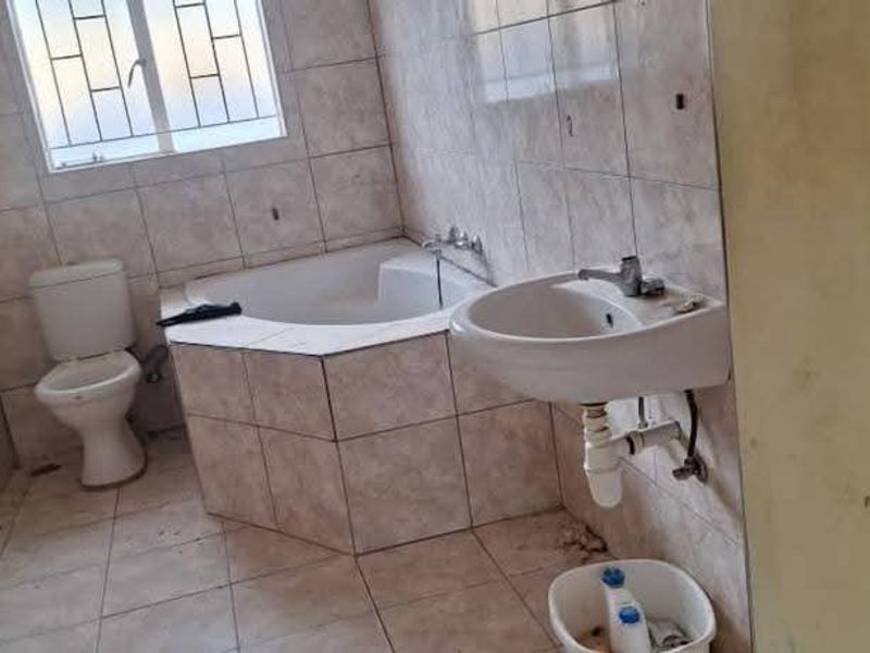 A functional bathroom featuring a built-in bathtub, pedestal washbasin, and toilet, finished with neutral ceramic wall and floor tiles.