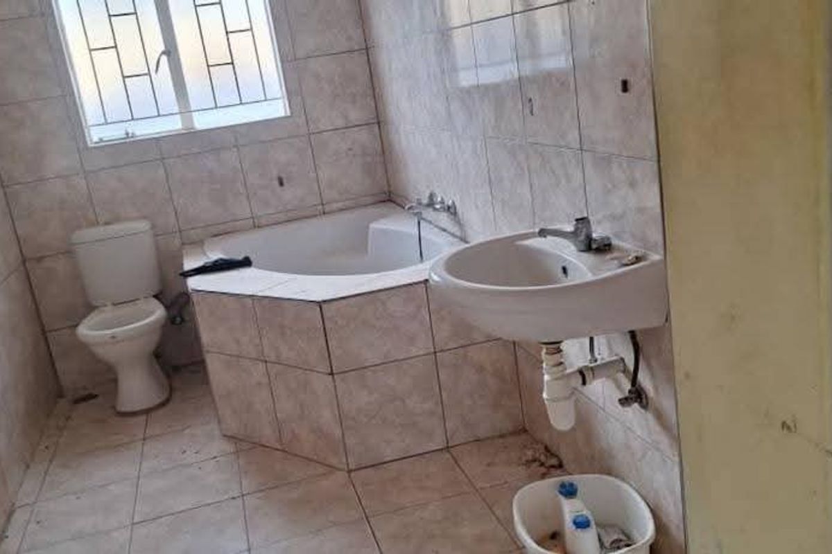 A functional bathroom featuring a built-in bathtub, pedestal washbasin, and toilet, finished with neutral ceramic wall and floor tiles.