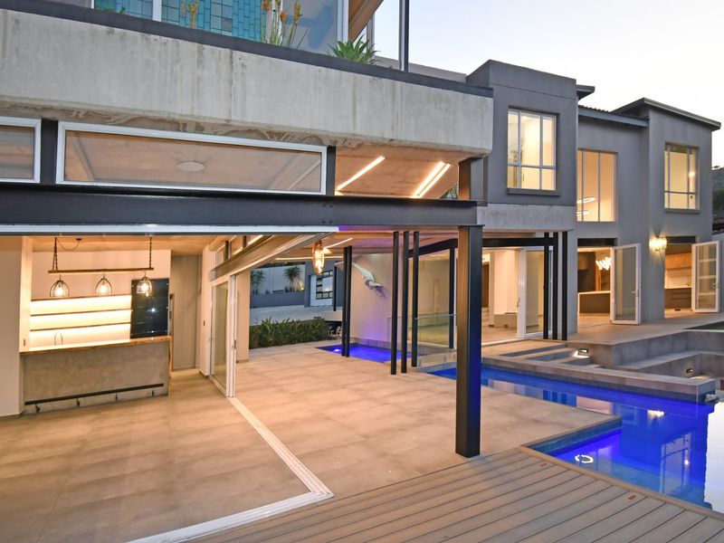 Modern covered patio area featuring a built-in bar, seamless indoor-outdoor flow, and direct access to a sleek swimming pool and timber deck.