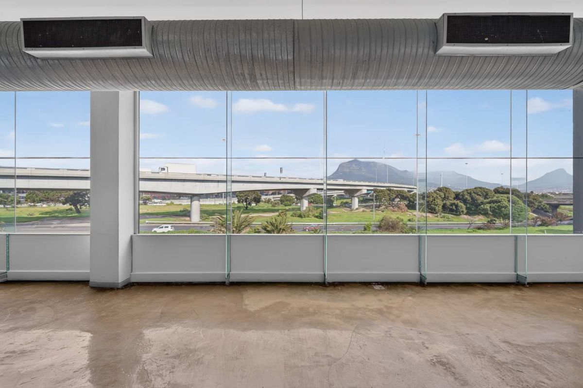 Open-plan office space featuring polished concrete floors, exposed industrial ducting, and expansive floor-to-ceiling windows offering scenic highway and mountain views.