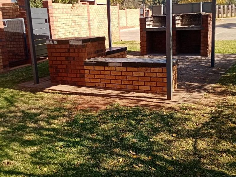 Outdoor entertainment area featuring a covered patio with a built-in brick braai and integrated brick seating, set within a private garden space.