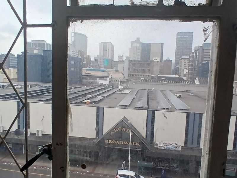 An elevated city view looking out through a weathered, metal-framed window over urban commercial buildings.