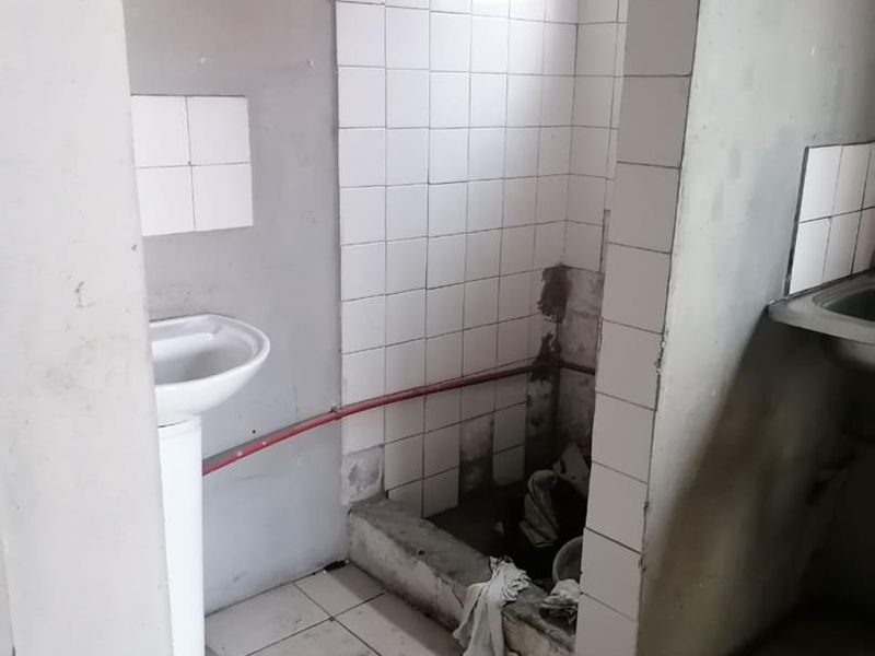 A small, unfinished bathroom space featuring a pedestal sink and a tiled shower area requiring significant repair and renovation to fixed finishes.