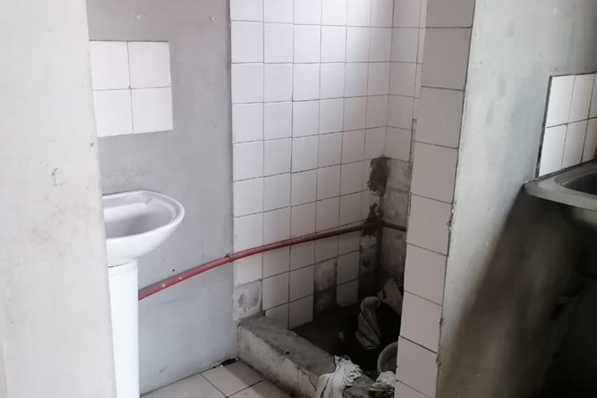 A small, unfinished bathroom space featuring a pedestal sink and a tiled shower area requiring significant repair and renovation to fixed finishes.