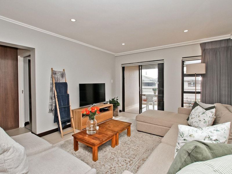 A bright and well-maintained living room featuring tiled flooring, recessed downlights, and a sliding glass door providing access to an outdoor balcony.