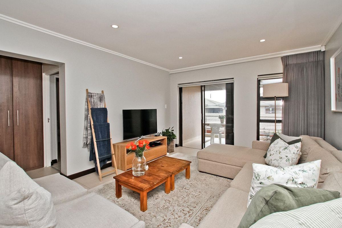 A bright and well-maintained living room featuring tiled flooring, recessed downlights, and a sliding glass door providing access to an outdoor balcony.