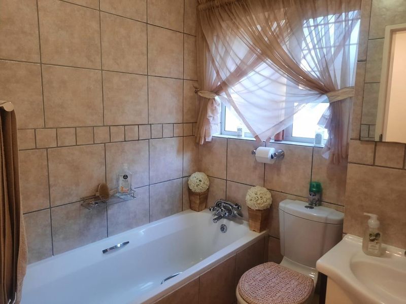 A functional bathroom featuring a built-in bathtub, ceramic wall tiling, a standard toilet, and a vanity basin with chrome fixtures.