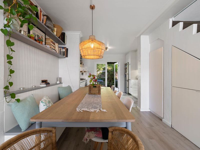 Open plan dining area featuring built-in bench seating, custom shelving, and under-stair storage, leading through to a bright kitchen and rear garden access.