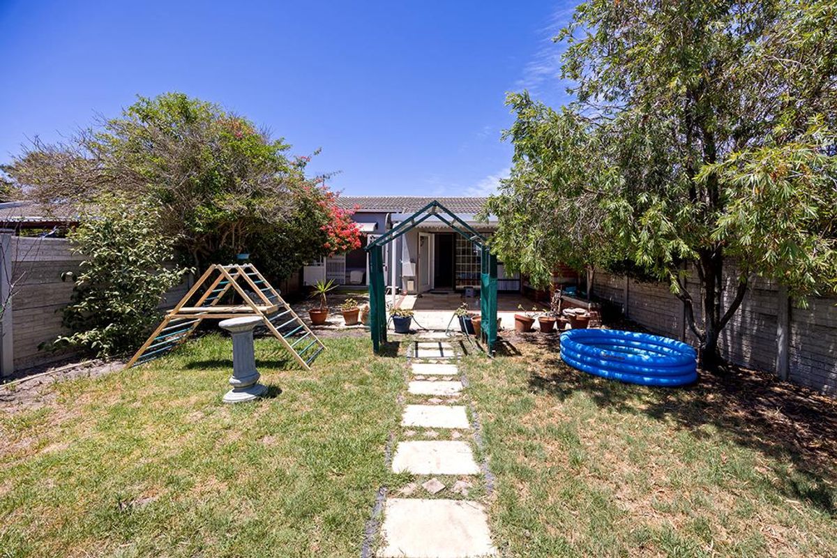 A rear garden featuring a paved walkway leading to a covered patio area, enclosed by precast concrete boundary walls.