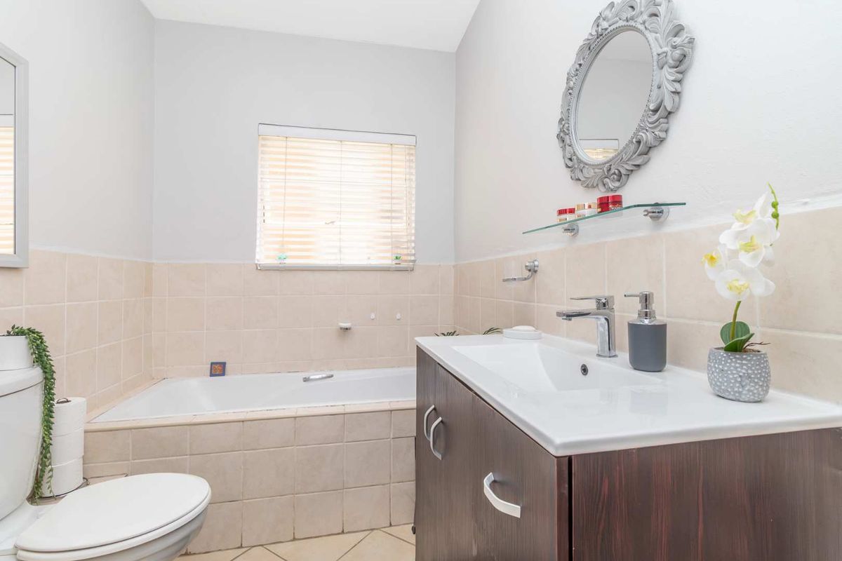 A functional bathroom featuring a built-in bathtub, a vanity cabinet with a basin, and neutral wall tiling.