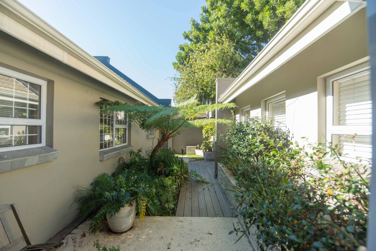A landscaped rear courtyard area featuring timber decking, concrete paving, and established garden beds between two building wings.