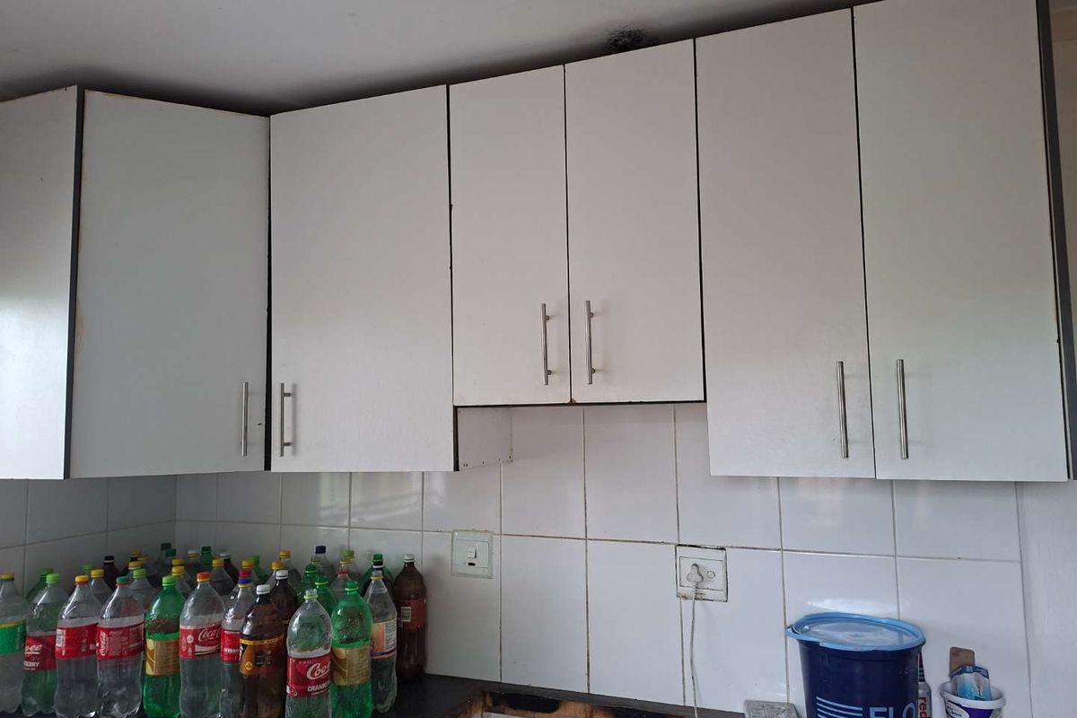 A kitchen area featuring white wall-mounted cabinetry and a tiled backsplash, currently requiring repairs to the base cabinetry and countertop area.