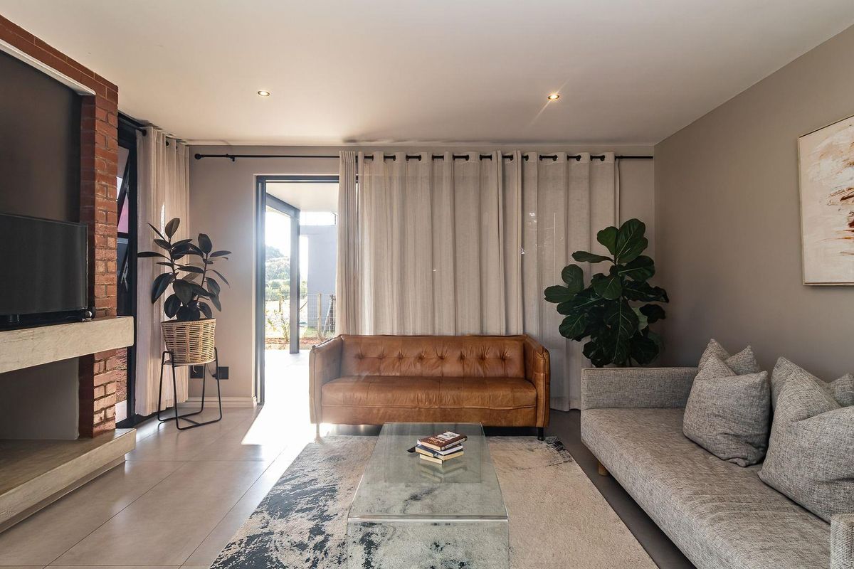 A modern living room featuring a prominent exposed brick fireplace, tiled flooring, and large sliding doors providing access to the outdoor patio area.
