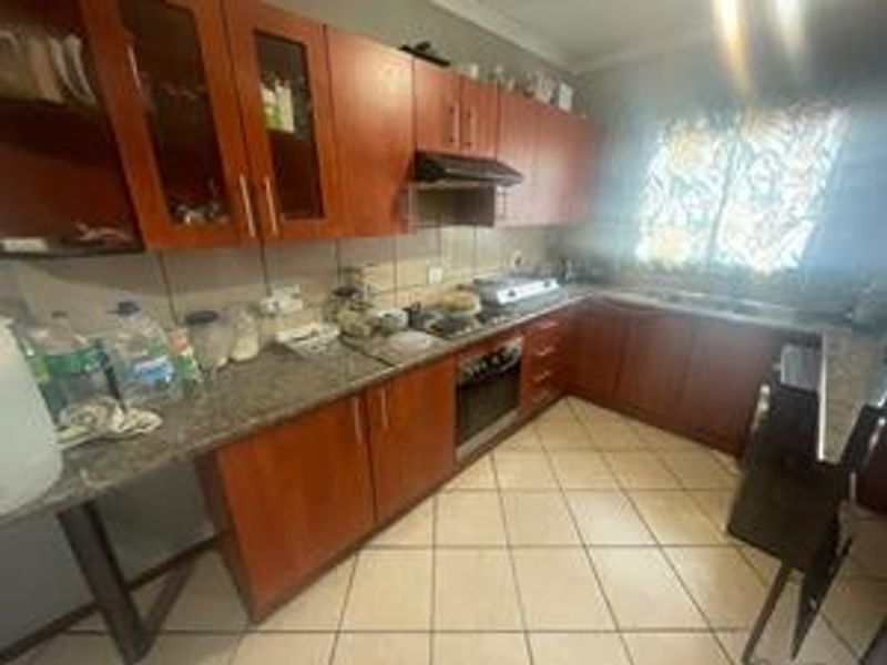 A functional kitchen featuring wooden cabinetry, granite countertops, a built-in oven, hob, and extractor fan with tiled flooring.