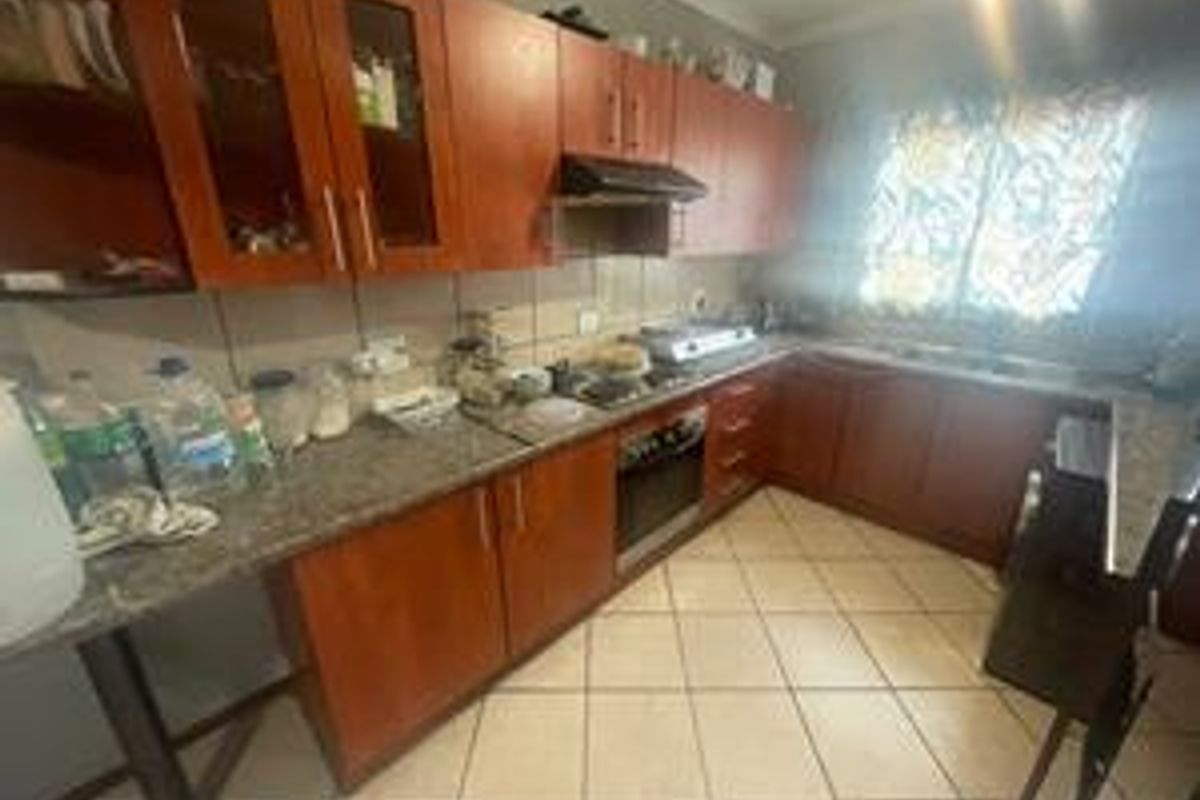 A functional kitchen featuring wooden cabinetry, granite countertops, a built-in oven, hob, and extractor fan with tiled flooring.