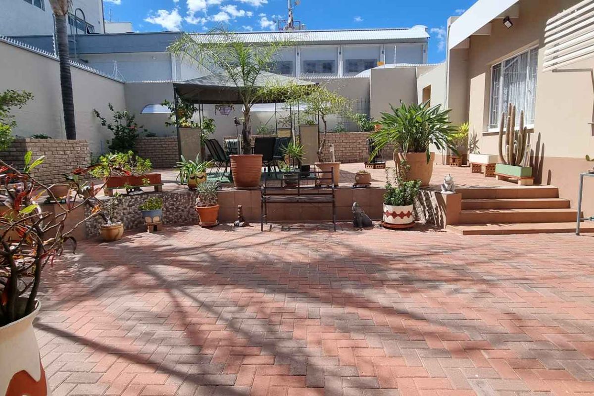 A paved rear courtyard featuring tiered levels, brick retaining walls, and a covered outdoor seating area, providing a functional space for outdoor relaxation.