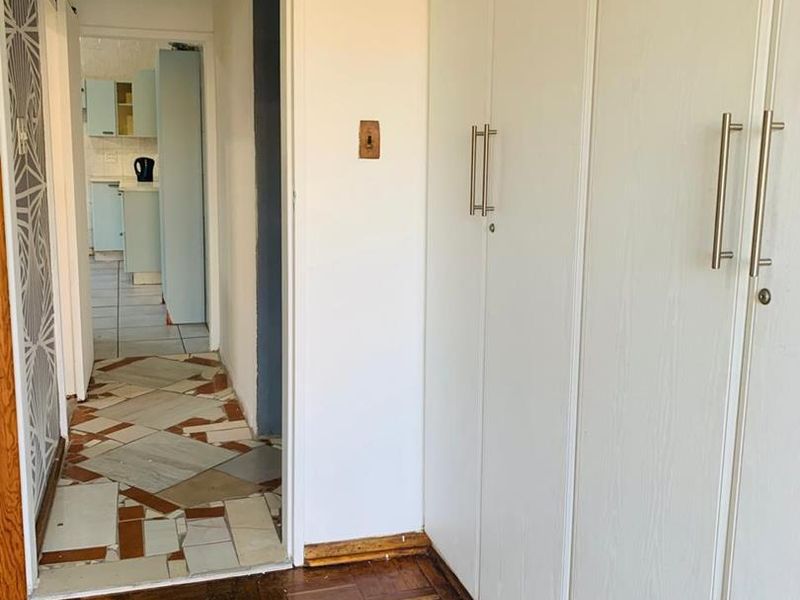 A hallway featuring built-in white cupboards, parquet flooring, and a view through to the kitchen area with tiled flooring.