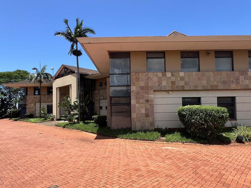 Front exterior view of a professional office building featuring stone cladding, large windows, and an extensive paved driveway with covered parking.