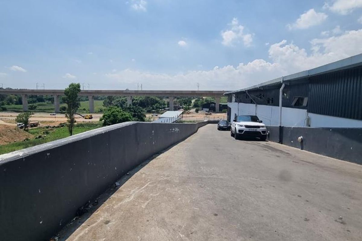 An exterior view of a concrete ramp leading up to a commercial building with metal cladding and a retaining wall.
