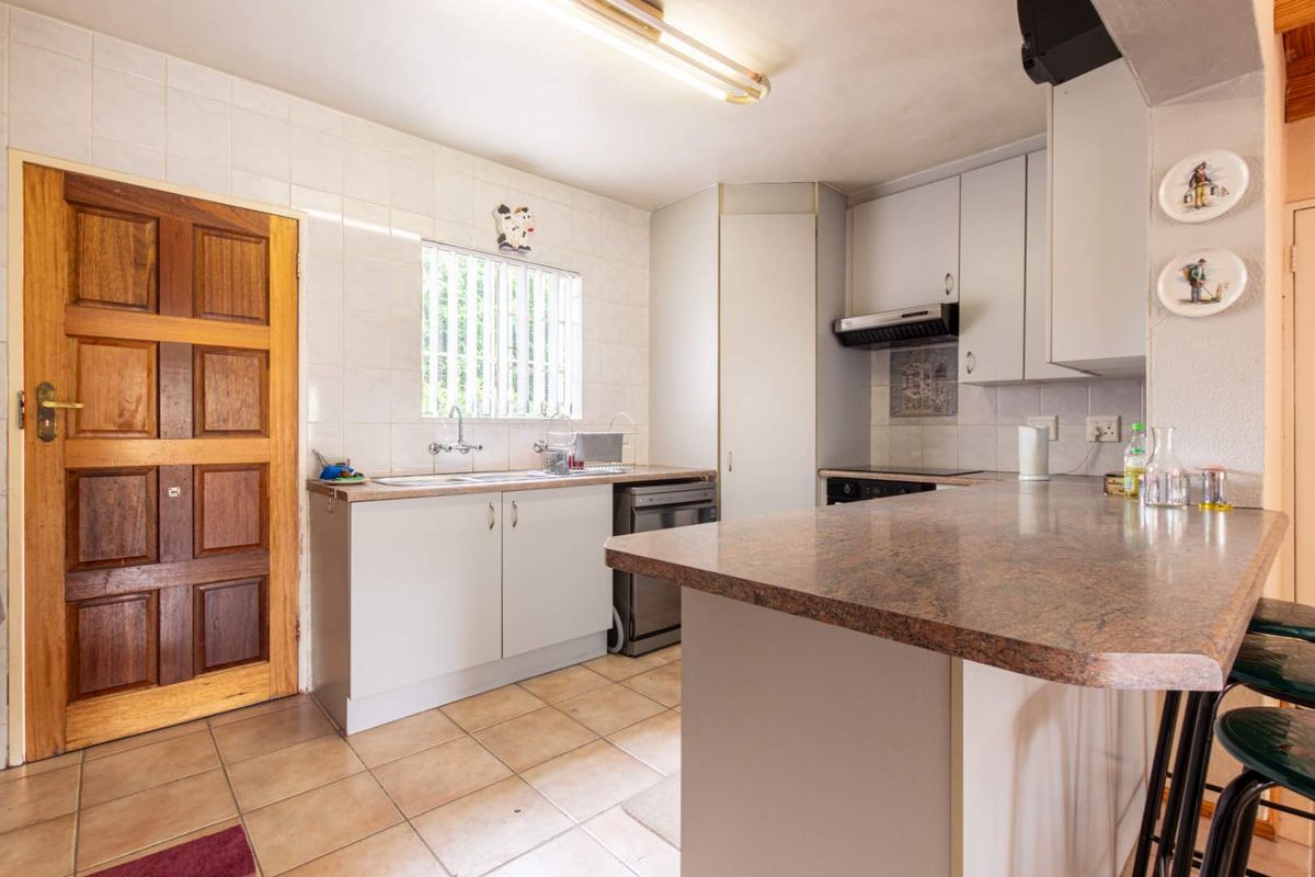 A functional kitchen featuring laminate countertops, built-in cabinetry, a stainless steel sink, and tiled flooring, offering a practical layout for daily meal preparation.